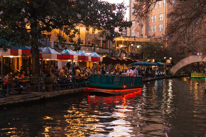 People eating and enjoying a guided cruise on the San Antonio River Walk in Texas at night time.