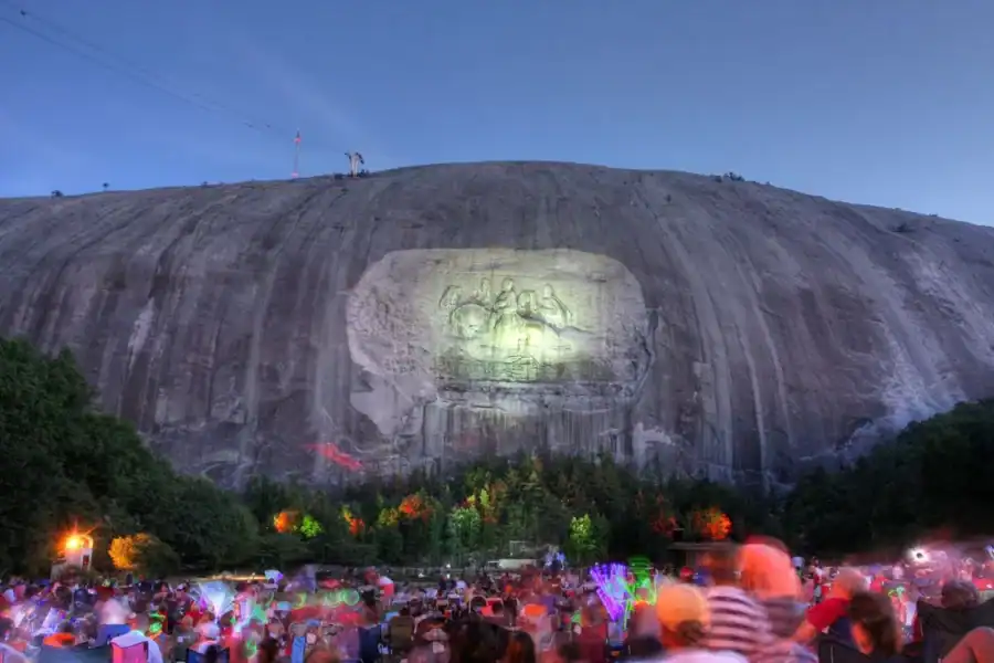 Stone Mountain in Atlanta lit up at night with lots of people watching fireworks.